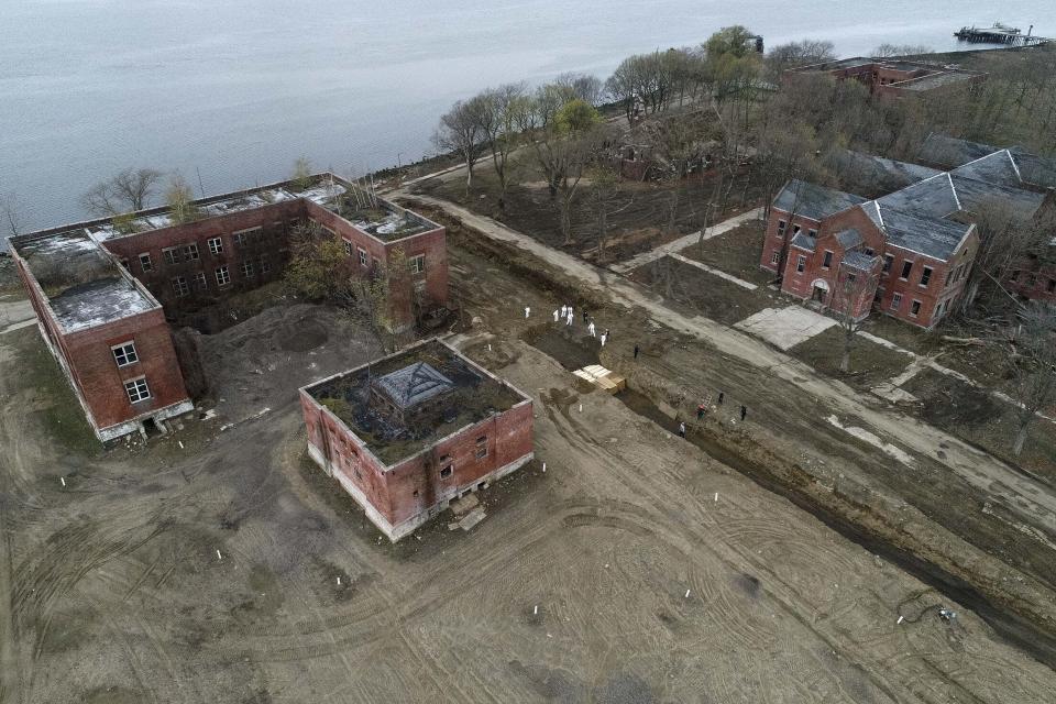 Workers wearing personal protective equipment bury bodies in a trench on Hart Island, Thursday, April 9, 2020, in the Bronx borough of New York. On Thursday, New York City’s medical examiner confirmed that the city has shortened the amount of time it will hold on to remains to 14 days from 30 days before they will be transferred for temporary internment at a City Cemetery. Earlier in the week, Mayor Bill DeBlasio said that officials have explored the possibility of temporary burials on Hart Island, a strip of land in Long Island Sound that has long served as the city’s potter’s field. (AP Photo/John Minchillo)