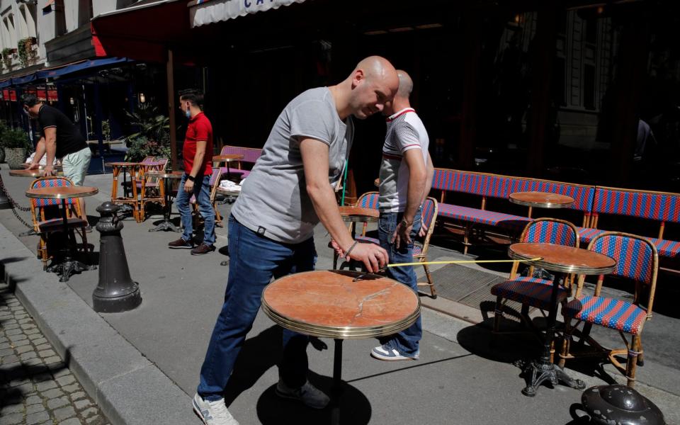 Waiters prepare tables on the terrace at a Parisian cafe, with each table placed apart in accordance with social distancing guidelines - Christophe Ena/AP