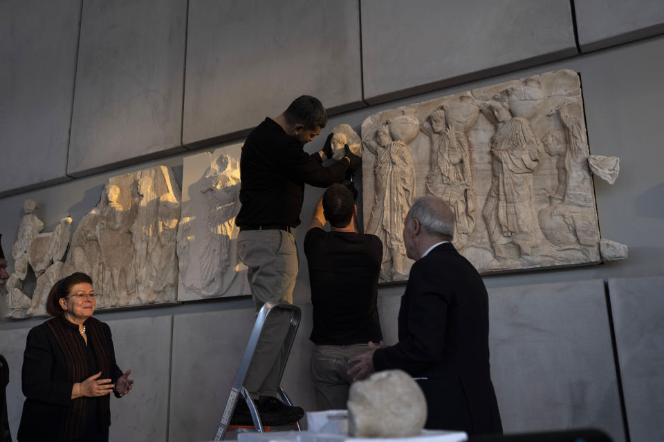 Acropolis Museum staff place a male head on the frieze of the Acropolis museum as Greek Culture Minister Lina Mendoni, left, looks on during a ceremony for the repatriation of three sculpture fragments, in Athens, on Friday, March 24, 2023. Greece received three fragments from the ancient Parthenon temple that had been kept at Vatican museums for two centuries. Culture Ministry officials said the act provided a boost for its campaign for the return of the Parthenon Marbles from the British Museum in London.(AP Photo/Petros Giannakouris)