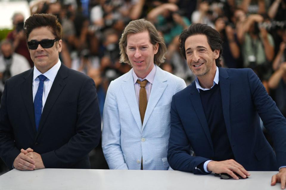 wes anderson, wearing a light blue suit, smiles next to adrian brody, who wears a dark blue suit jacket and black shirt