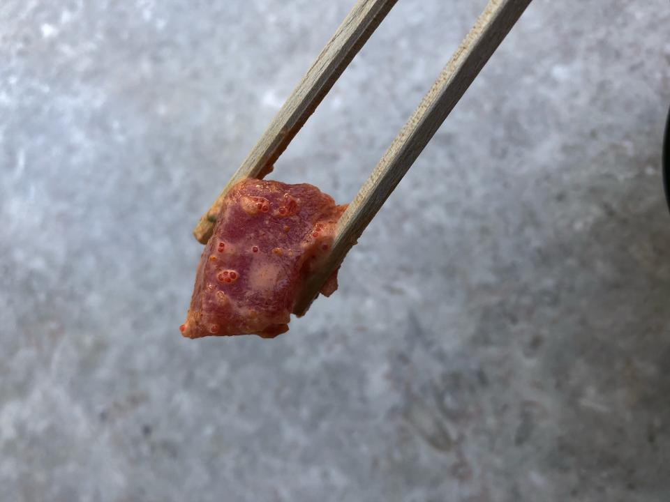 A piece of fish from a spicy ahi poke bowl, held by chopsticks against a stone table background