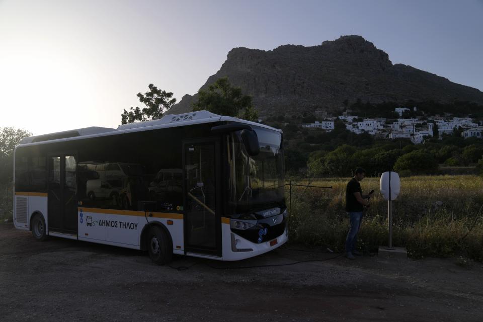 Deputy Mayor Spyros Aliferis charges the electricity municipal bus on the Aegean Sea island of Tilos, southeastern Greece, Monday, May 9, 2022. When deciding where to test green tech, Greek policymakers picked the remotest point on the map, tiny Tilos. Providing electricity and basic services, and even access by ferry is all a challenge for this island of just 500 year-round inhabitants. It's latest mission: Dealing with plastic. (AP Photo/Thanassis Stavrakis)