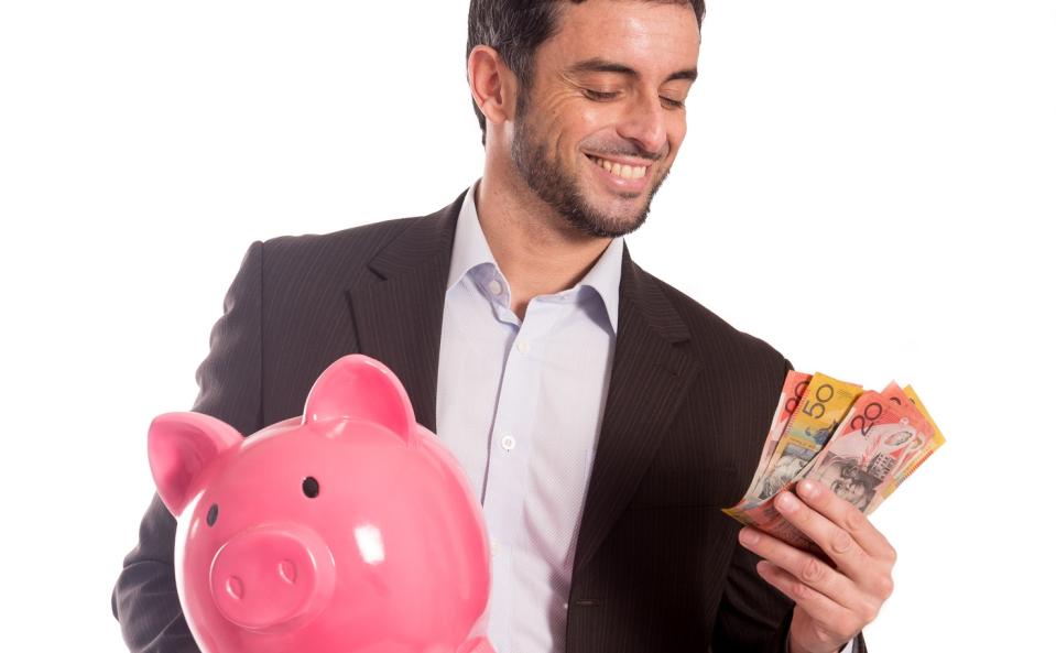 A man holding Australian banknotes smiling while holding a piggy bank in the other hand.