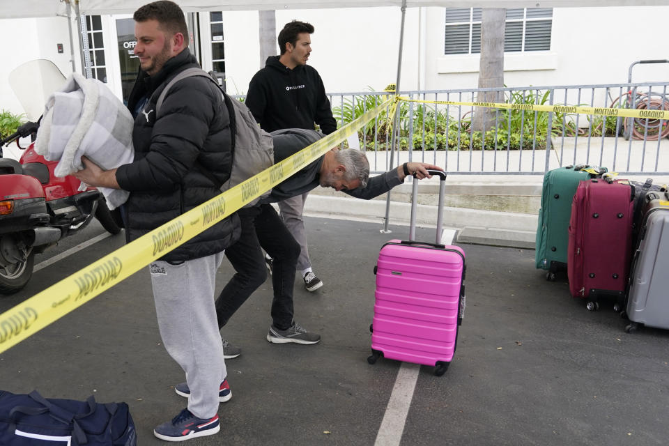 Phil Metzger, center, of the Christian church Calvary San Diego, ducks under tape as he helps Ukrainians arriving after crossing into the United States from Tijuana, Mexico, Friday, April 1, 2022, in Chula Vista, Calif. (AP Photo/Gregory Bull)