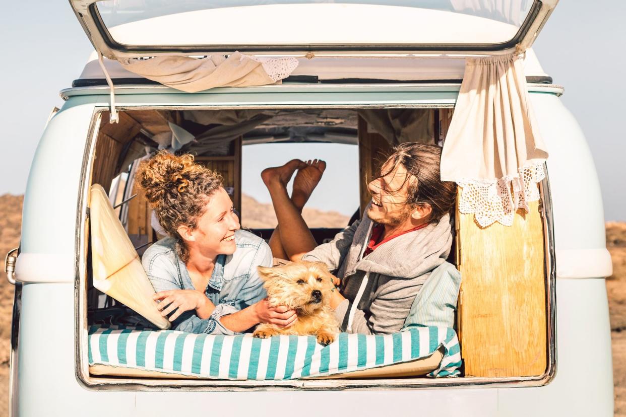 dog enjoying his summer vacation in the back of a vintage van with a woman and a man