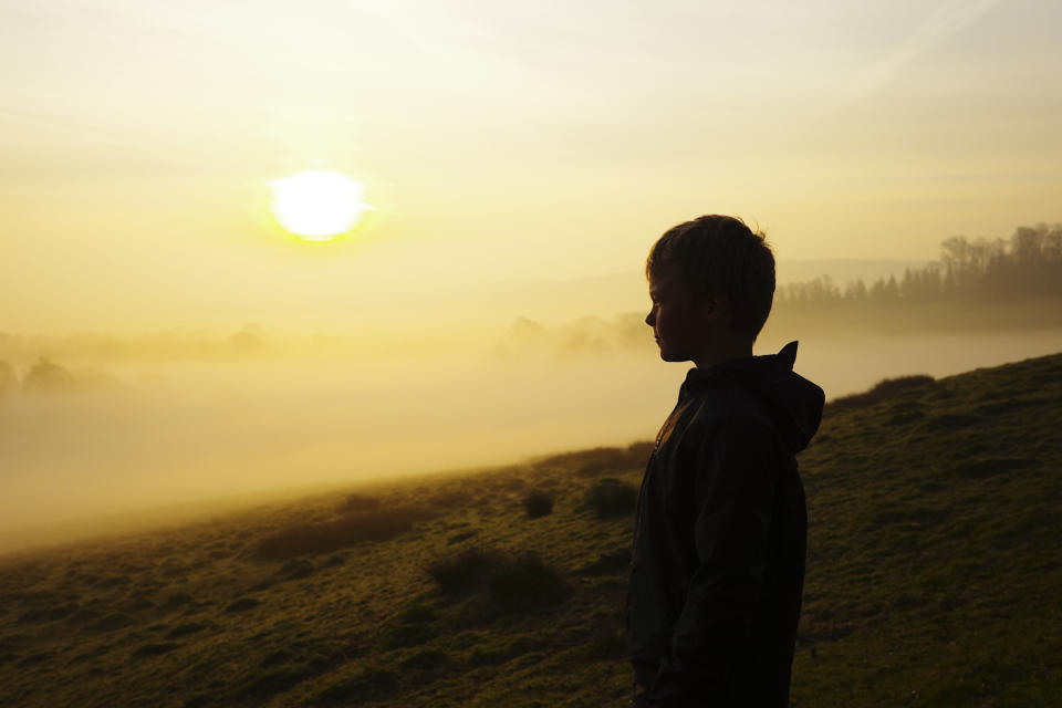 Boy looking out over a misty vista at sunrise