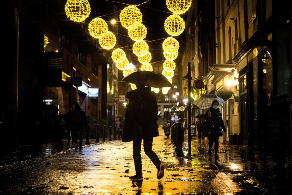 A man crosses a quiet street filled with Christmas lights in central London, Monday November 9, 2020. Wet weather has drenched the London streets during the first full week of a four-week coronavirus lockdown in England, as some are calling to allow businesses to open their doors to kickstart the city economy. (Victoria Jones/PA via AP)