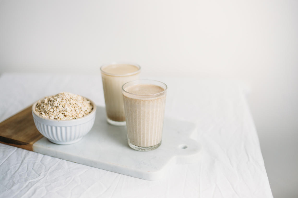 A bowl of uncooked oats and two glasses of what looks like oat milk.