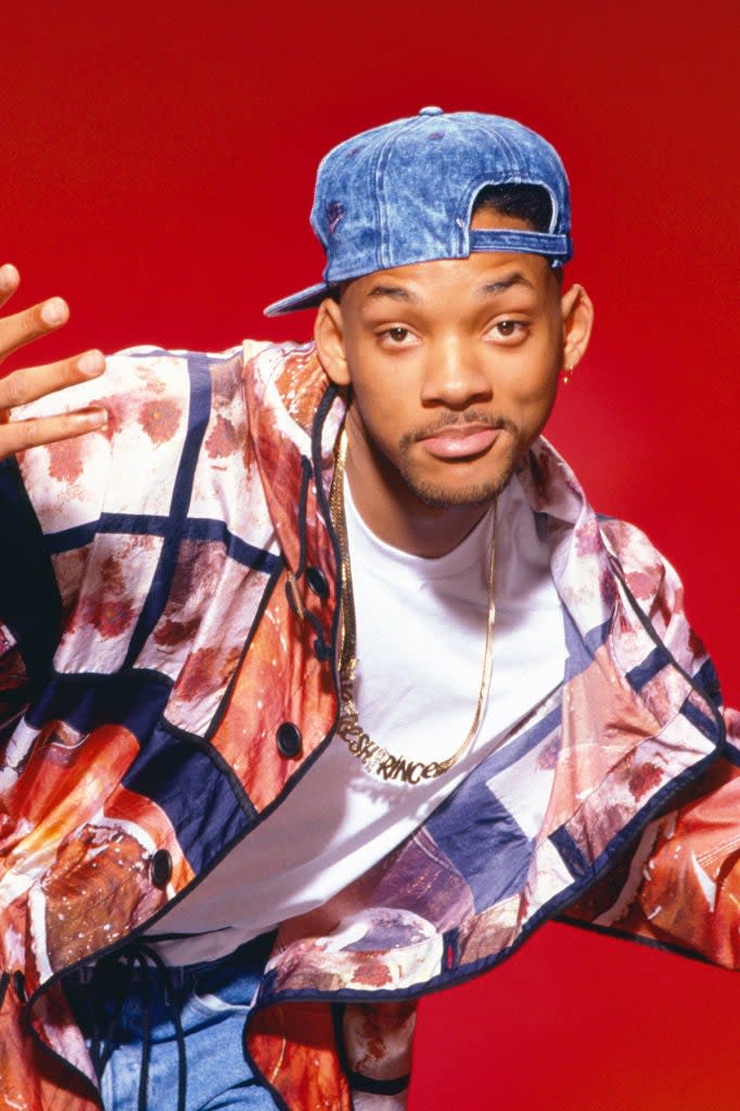 A person poses with a hand gesture, wearing a vibrant printed jacket and a cap