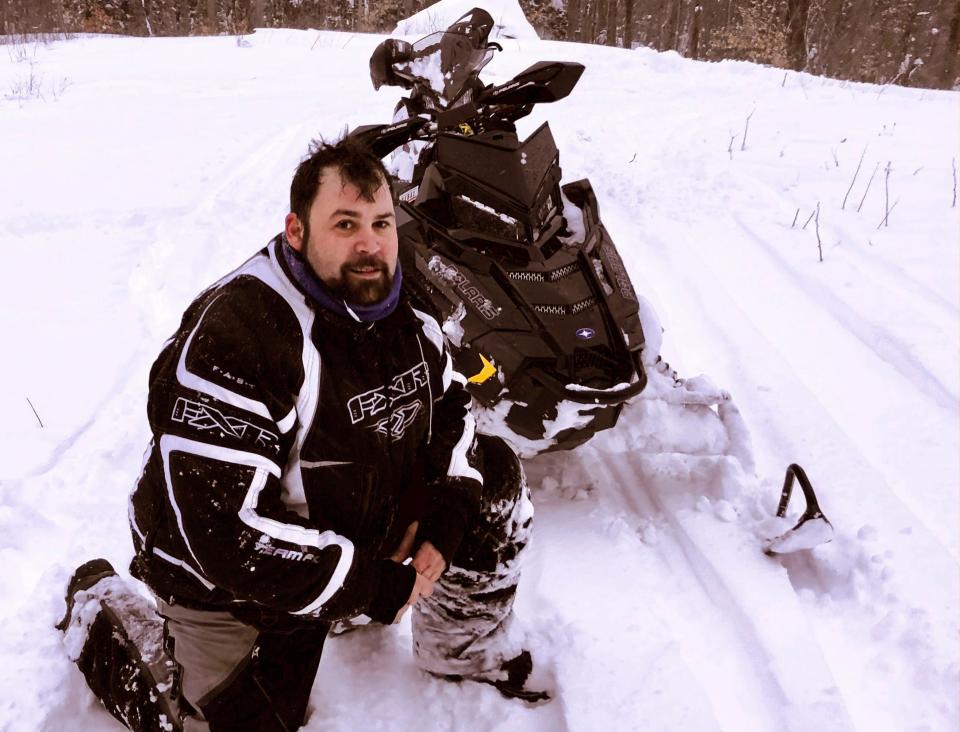 In this photograph provided by Richard Smith, Jeffrey Smith poses with a snowmobile during March 2018, in Windsor, Mass. Jeffrey Smith has filed suit against the government to pay nearly $10 million after being badly injured in a snowmobile crash in 2019 with a Black Hawk helicopter. Smith's snowmobile collided with a helicopter that was parked on a Massachusetts snow-covered trail at dusk. (Jeffrey Smith photo via AP)