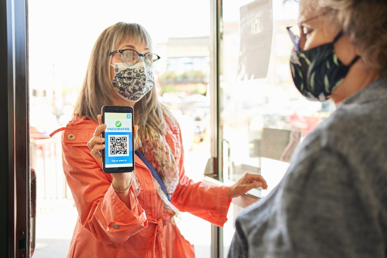 Mature woman wearing a protective face mask showing a store owner her Covid-19 pass on her phone at a shop entrance