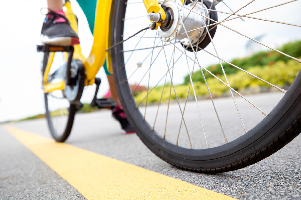 Close up of a woman pedaling a bicycle. Focus is on the bicycle wheel.