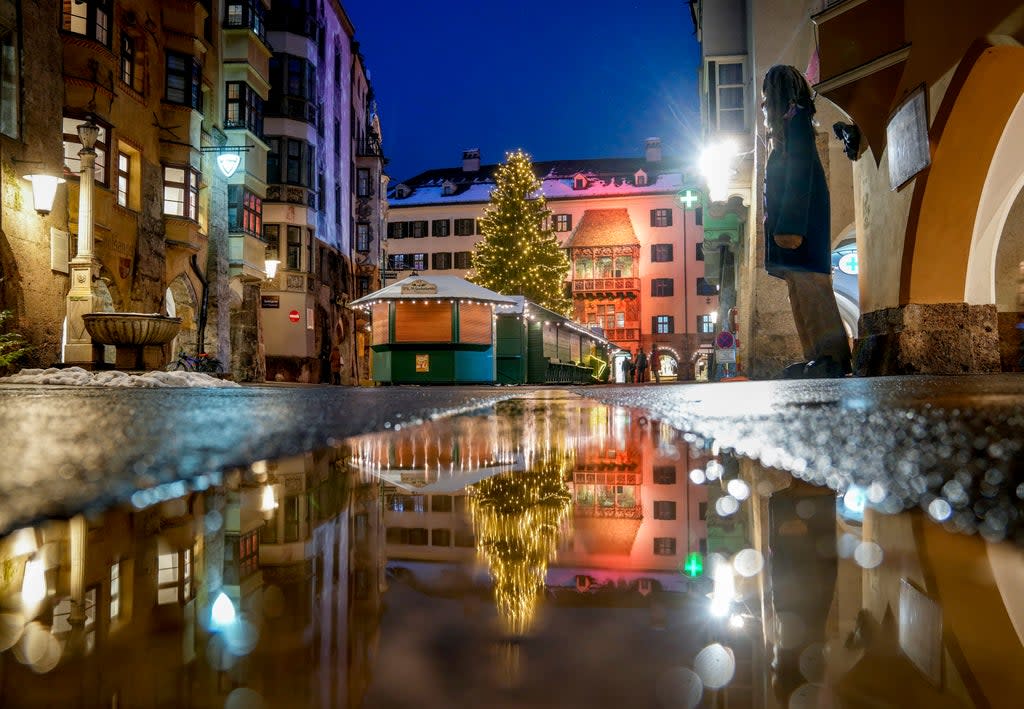 The Christmas tree of Innsbruck’s closed festive market is reflected in a puddle  (AP)