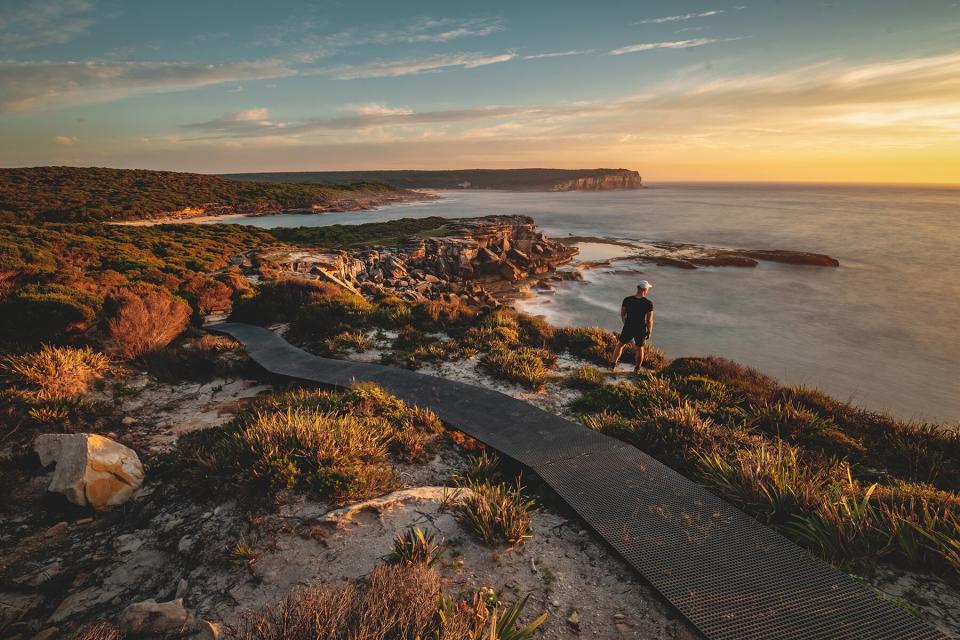 A man standing on a cliff in the Royal National Park during sunset