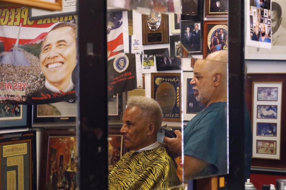 Lawrence Tolliver, reflected in a mirror, cuts a customer's hair in 2019.