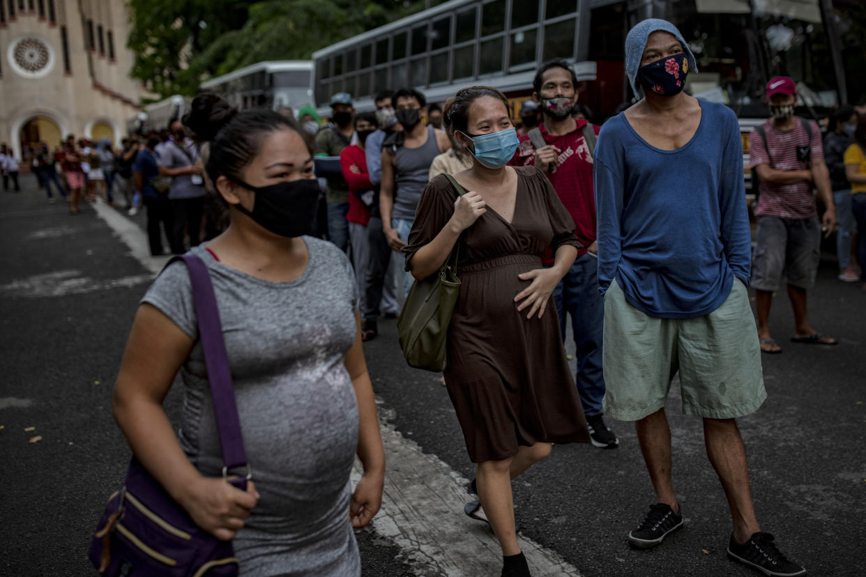Pregnant women walk past other Filipinos out of work and stranded due to the coronavirus pandemic as they queue to receive meals before taking a free bus ride home to their province on May 29, 2020 in Parañaque, Metro Manila, Philippines. (Photo by Ezra Acayan/Getty Images)
