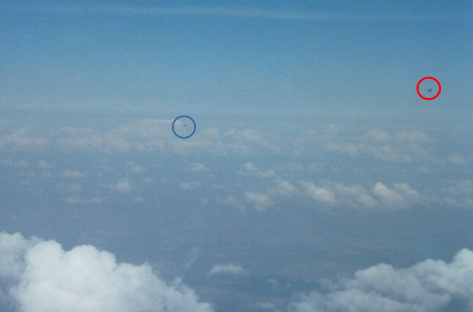 An appreciation of what air combat really looks like. I took this photo a few years after the events in this story. My wingman in the blue circle is another CF-18 flying over Germany, three miles away. The red circle is around a Luftwaffe F-4 Phantom, pulling up to attack. He is also about two miles away. The wing shape and smoke trail make identifying the F-4 easy. With my eyes (better perception than the camera), I could see his belly (no canopy), indicating he was turning away from me.