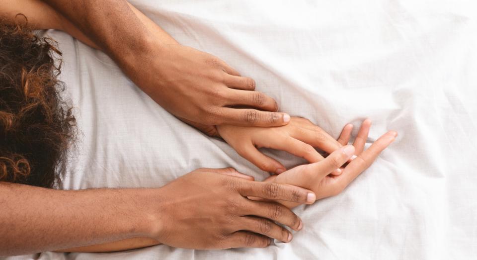 Man and women's hands on bed.