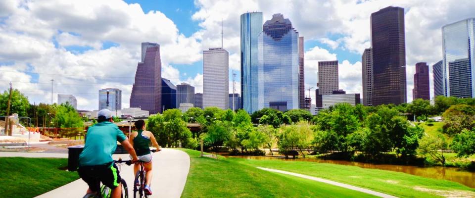 Riding Bikes on Paved Trail in Houston Park (view of river and skyline of downtown Houston) - Houston, Texas, USA