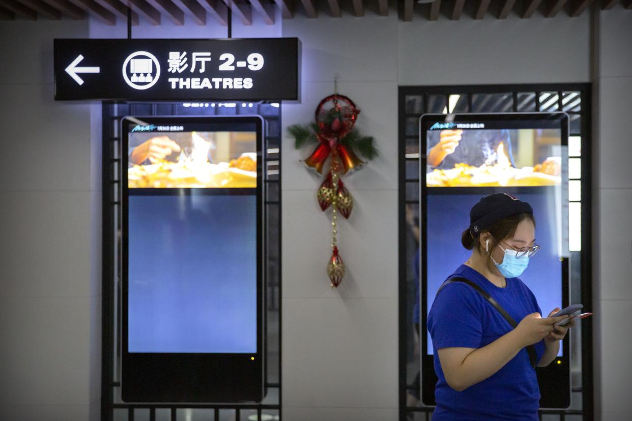 A patron wearing a face mask to protect against the coronavirus uses her smartphone in the lobby of a movie theater in Beijing on July 24, 2020.