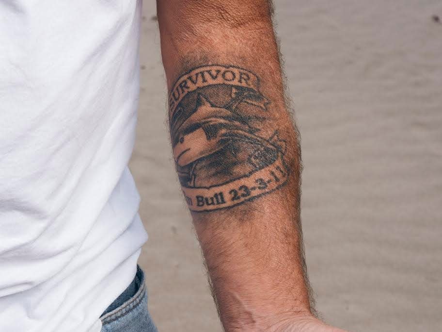 A photograph of a persons forearm with a tattoo that reads "survivor, bull shark, 23/2/11"