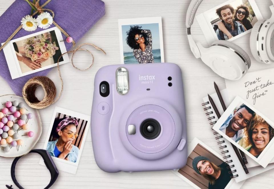 Purple mini camera surrounded by mini photos, white headphones, notebook, twine, and flowers