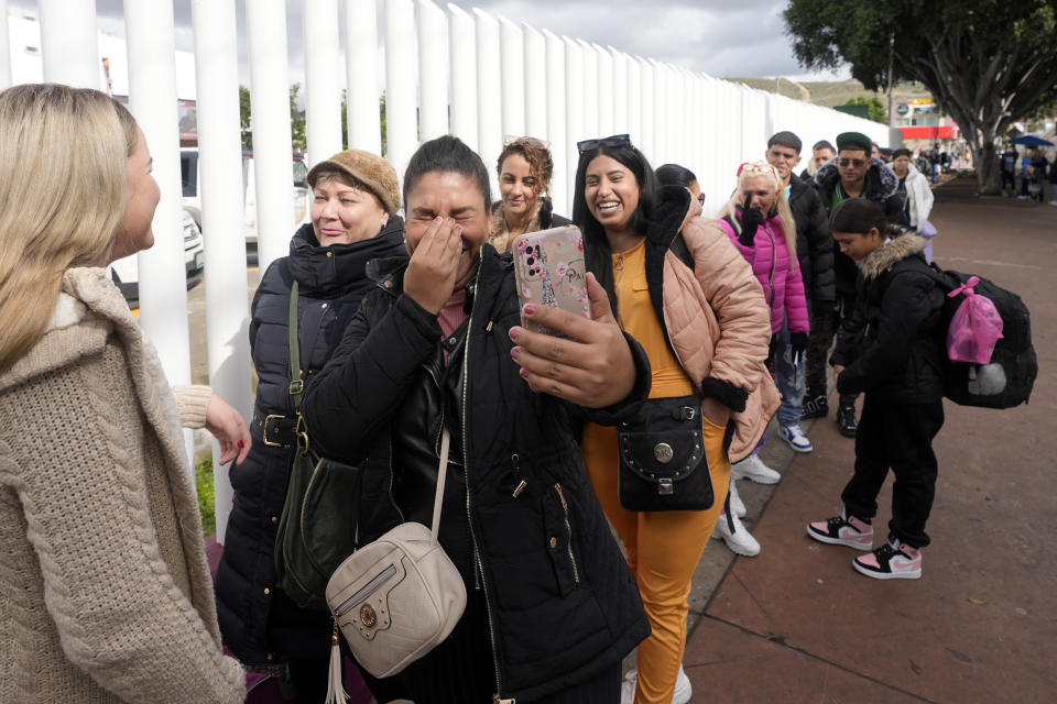 Women from Cuba laugh while connecting with family with a phone as they line up to cross into the United States for their appointment to seek asylum, Friday, Feb. 2, 2024, in Tijuana, Mexico. (AP Photo/Gregory Bull)