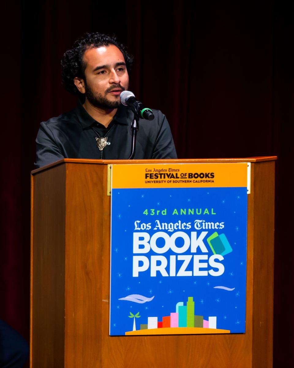 Man with curly hair behind a podium.