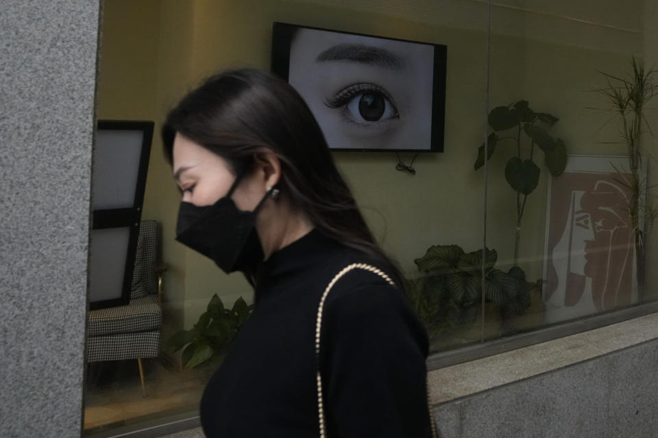 A woman wearing a mask walks past a beauty salon, Tuesday, June 28, 2022, in Beijing. (AP Photo/Ng Han Guan)