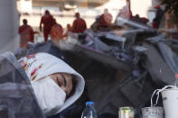 A local resident, staying outdoors for fear of aftershocks, takes.a moment to relax inside a coffee shop, as members of rescue services searching for survivors in the debris of a collapsed building are reflected in the window, in Izmir, Turkey, early Saturday, Oct. 31, 2020. Rescue teams on Saturday ploughed through concrete blocs and debris of eight collapsed buildings in Turkey's third largest city in search of survivors of a powerful earthquake that struck Turkey's Aegean coast and north of the Greek island of Samos, killing dozens Hundreds of other were injured. (AP Photo/Darko Bandic)