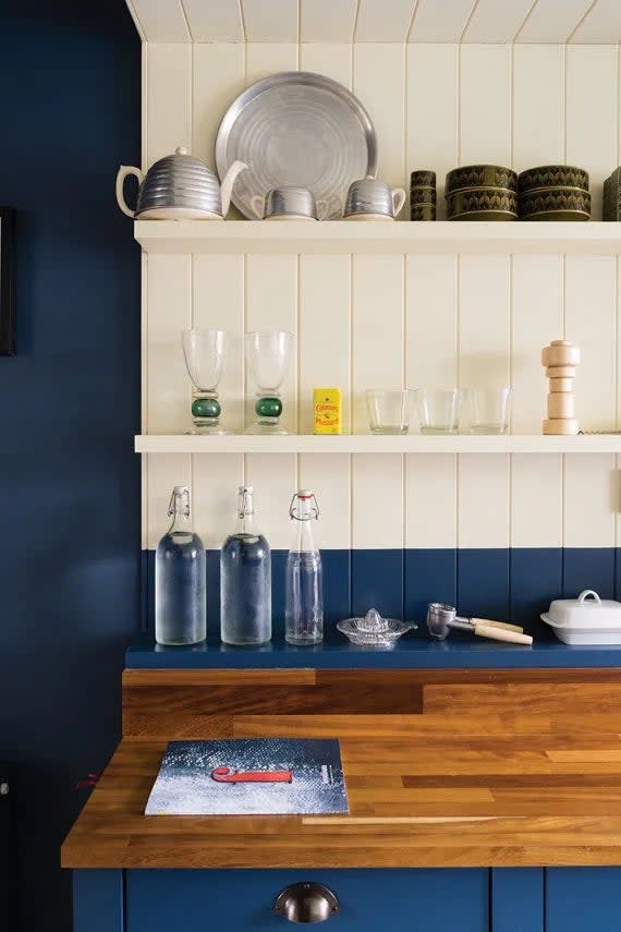A blue kitchen wall with a white open shelving, the latter painted with 