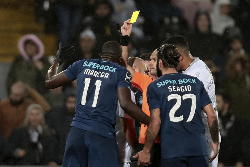 Referee Luis Godinho shows a yellow card to Porto's Moussa Marega, left, during a Portuguese league soccer match between Vitoria SC and FC Porto in Guimaraes, Portugal, Sunday, Feb. 15, 2020. The president and the prime minister of Portugal have added their voices to a national outcry over racist abuse aimed at Moussa Marega who walked off the field after hearing monkey chants. (AP Photo)