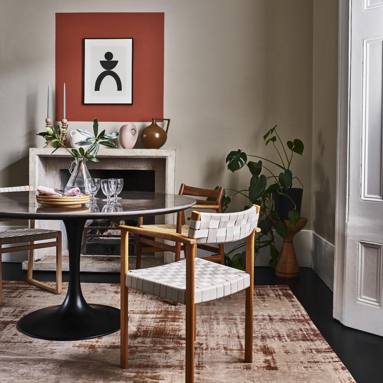  A dining room with a round dining table and woven chairs atop a patterned rug. 