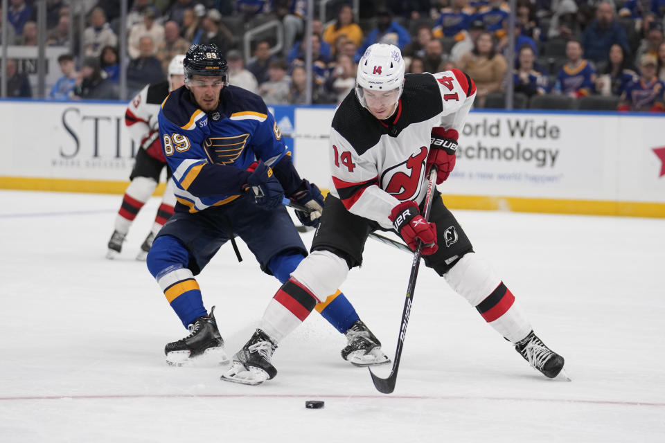 New Jersey Devils' Nathan Bastian (14) and St. Louis Blues' Pavel Buchnevich (89) battle for a loose puck during the third period of an NHL hockey game Friday, Nov. 3, 2023, in St. Louis. (AP Photo/Jeff Roberson)