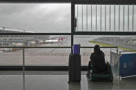 A passenger sits on her luggage watching passenger airplanes parked on the tarmac after all flights were canceled at Pudong International Airport in Shanghai, China, Sunday, July 25, 2021. Airline flights were canceled in eastern China and cargo ships were ordered out of the area Saturday as Typhoon In-fa churned toward the mainland after dumping rain on Taiwan. (AP Photo/Andy Wong)