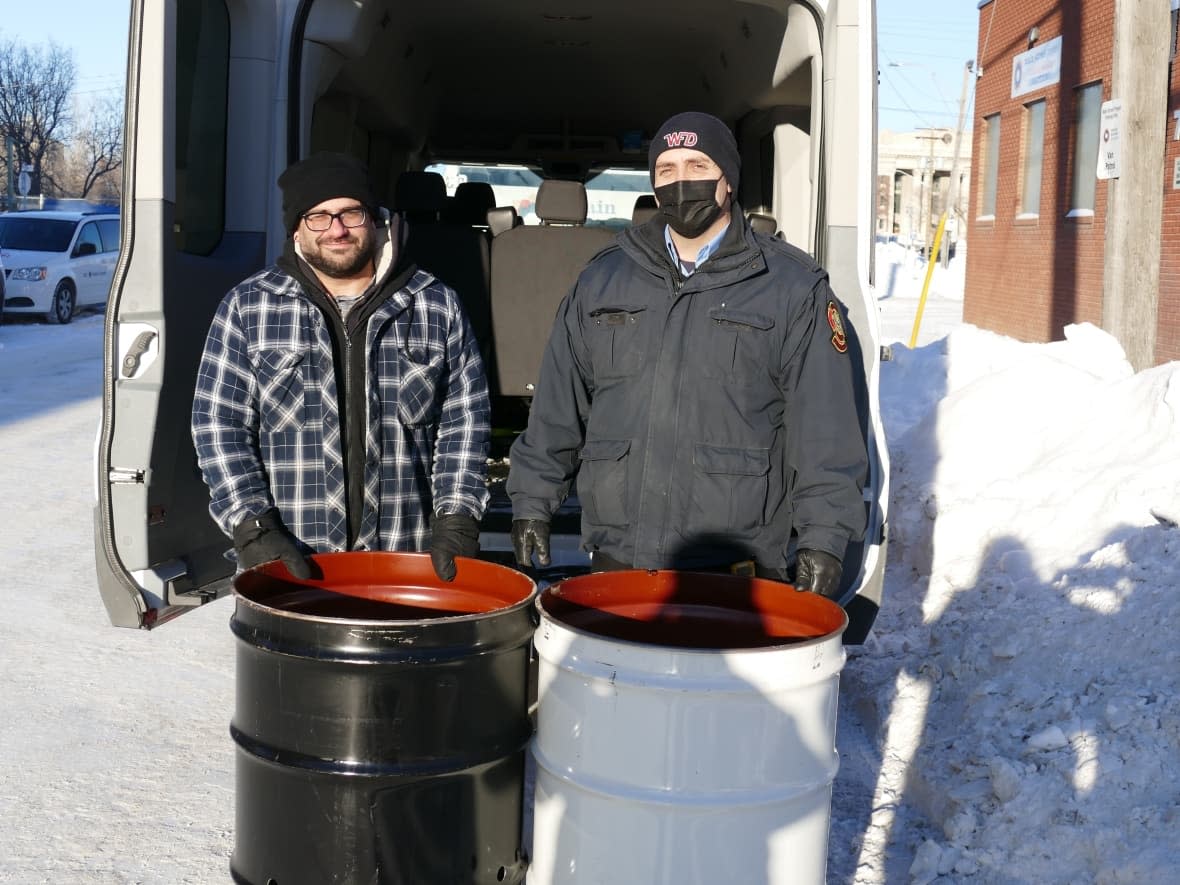 Shawn Sousa, left, outreach services manager at Main Street Project, and Steve Antle, a fire prevention officer with Winnipeg Fire Paramedic Services stand with two of 15 burn barrels that are being placing at different homeless camps around the city. (Jeff Stapleton/CBC - image credit)