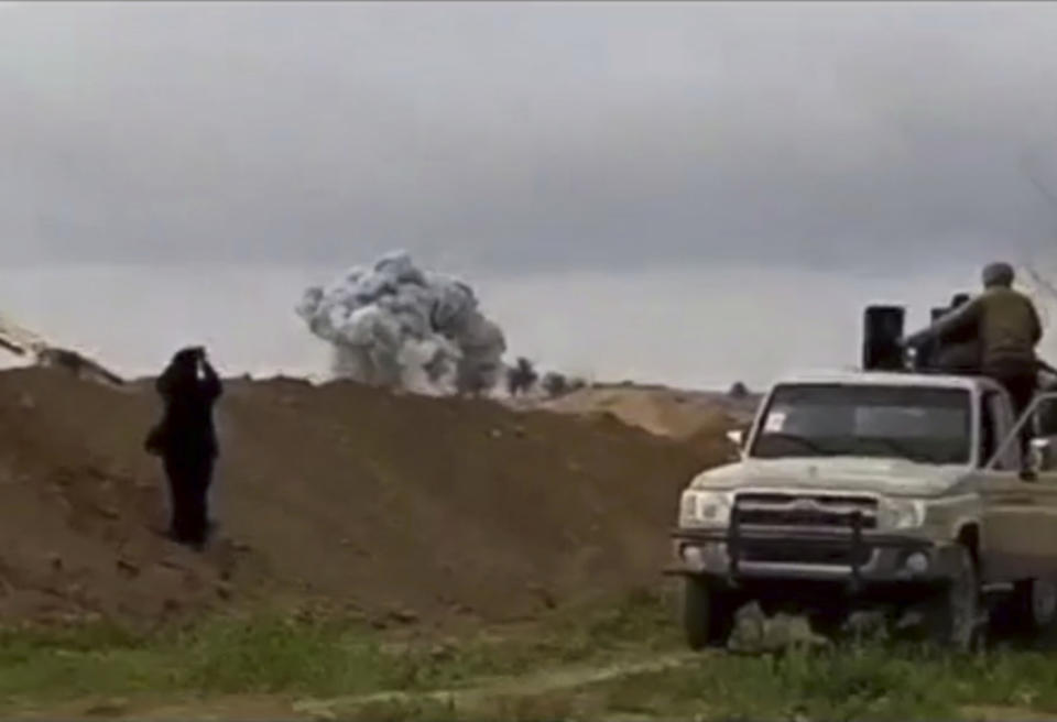This frame grab from video provided Tuesday, Feb. 12, 2019, by the Syrian Observatory for Human Rights, an opposition group, that is consistent with independent AP reporting, shows U.S.-backed Syrian Democratic Forces fighters looking at smoke rising from a shell that targeted Islamic State group militants, in the village of Baghouz, Deir El-Zour, eastern Syria. Fighting between U.S.-backed fighters and IS inflicted more casualties among people fleeing the violence in eastern Syria Tuesday where the extremists are on the verge of losing the last area they control. (Syrian Observatory for Human Rights via AP)