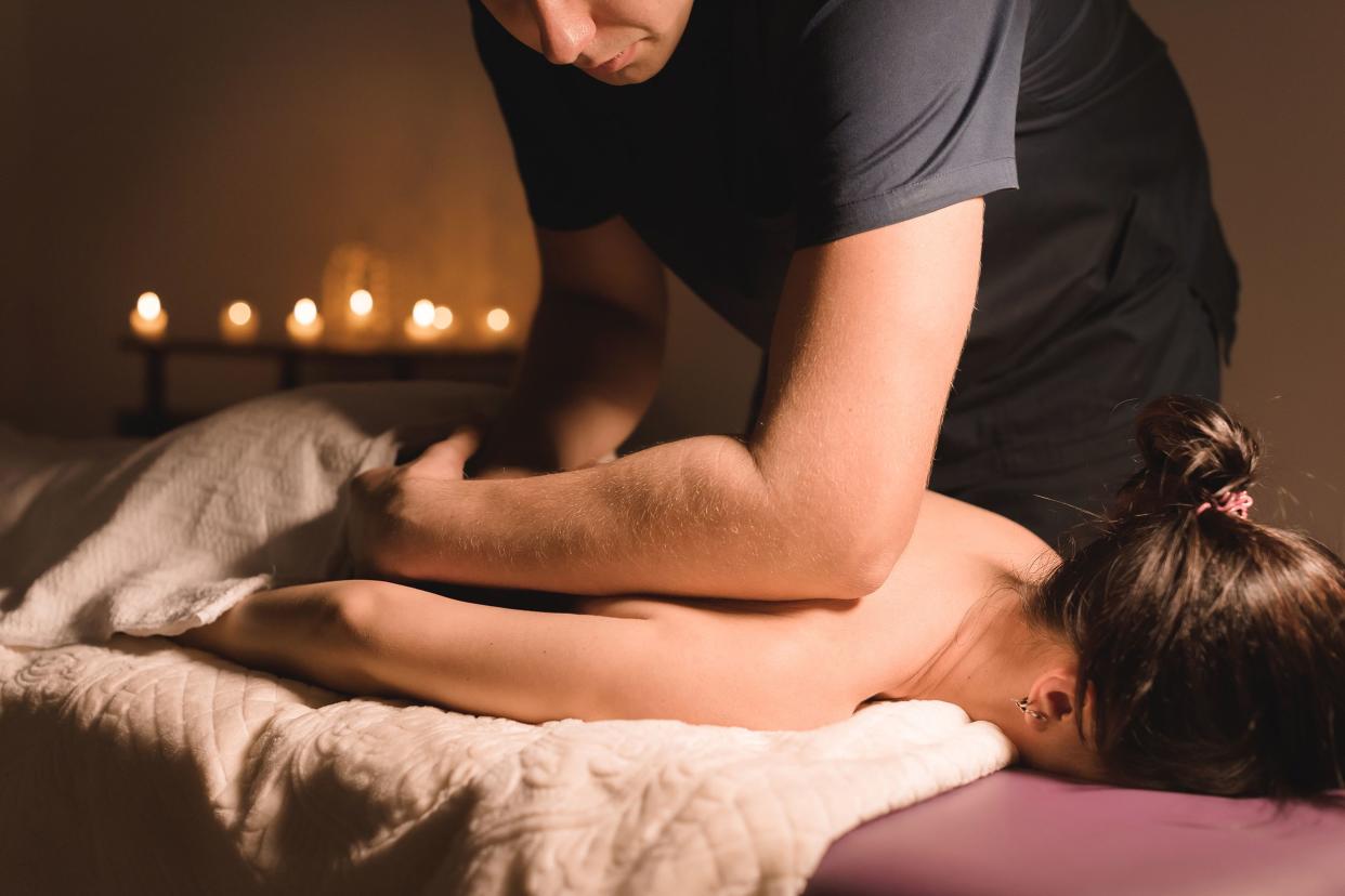 male massage therapist doing a back and shoulder massage to a woman