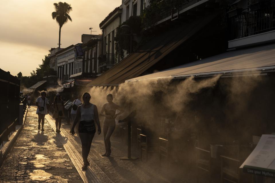 FILE - People walk next a mist machine to cool down, in Monastiraki district of Athens, on Thursday, July 20, 2023. Rising global temperatures are elevating air conditioning from a luxury to a necessity in many parts of Europe, which long has had a conflictual relationship with energy-sucking cooling systems deemed by many a U.S. indulgence. (AP Photo/Petros Giannakouris, file)