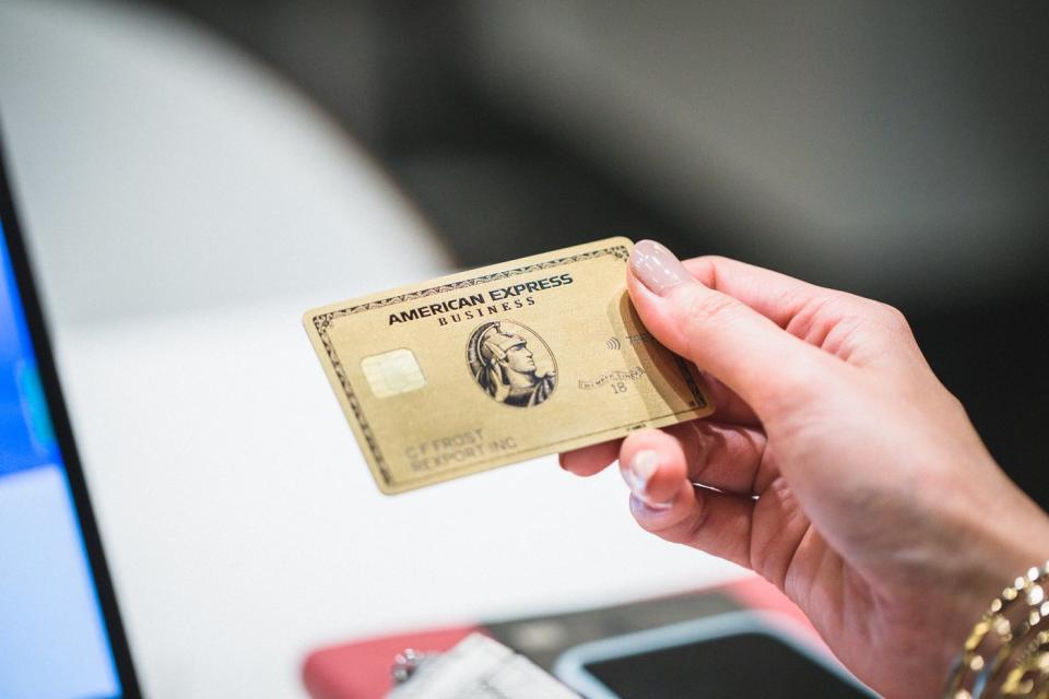 A person holding a gold American Express business credit card in his right hand.