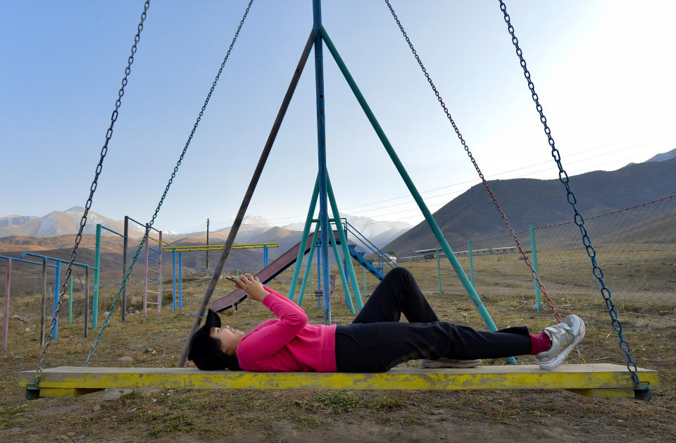 Kanat Kaliyev's daughter Malika plays with her phone lying on a swing near their family house in the village of Tash-Bashat about 24 kilometers (15 miles) southeast of Bishkek, Kyrgyzstan, Saturday, Oct. 17, 2020. Kyrgyzstan, one of the poorest countries to emerge from the former Soviet Union, saw its president forced out by protesters earlier this month, but the political turmoil hasn't touched that village nestled in the scenic Ala-Too mountains where life follows centuries-old rites. (AP Photo/Vladimir Voronin)