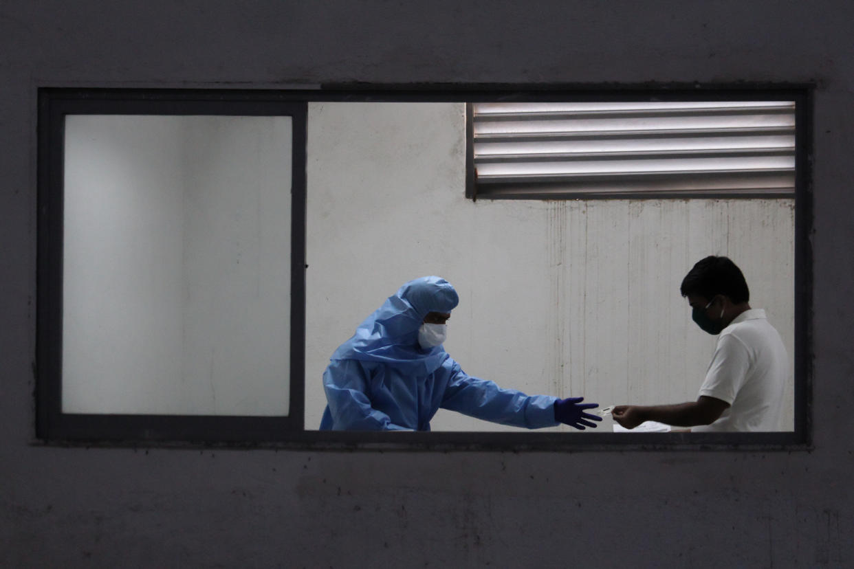 A healthcare worker wearing personal protective equipment (PPE) checks documents of a man during a medical check-up in Mumbai, India on July 27, 2020. India has become the third country after the United States and Brazil, to cross 01 million COVID-19 cases. (Photo by Himanshu Bhatt/NurPhoto via Getty Images)