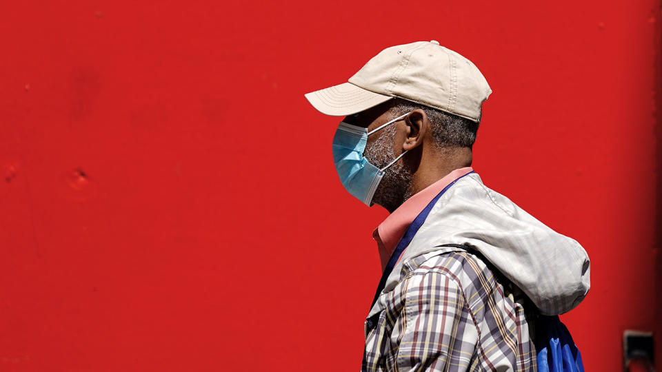 A pedestrian in a baseball cap and a plaid jacket with a hood is shown against a bright red background. 