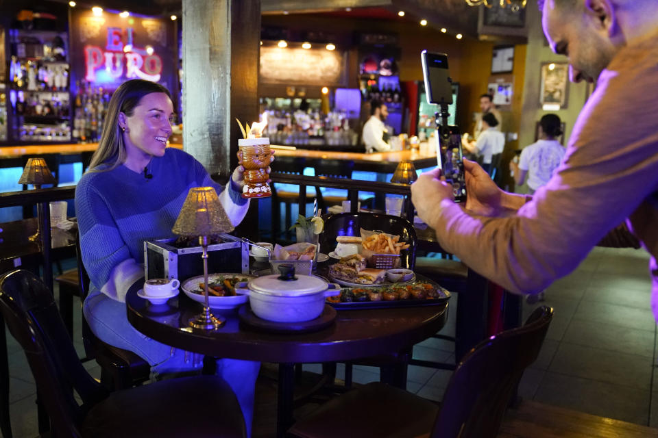 Content creator Jensen Savannah, left, and her fiance and brand manager Jorge Millares, produce a client video at El Puro Cuban Restaurant, Thursday, March 14, 2024, in Charlotte, N.C. (AP Photo/Erik Verduzco)