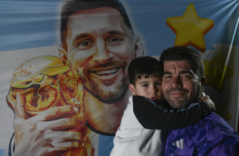 El aficionado argentino Matías Celestino y su hijo Benito Lionel posan para una foto frente a una bandera con l imagen de Lionel Messi en su residencia en Buenos Aires, Argentina, el lunes 3 de junio de 2024. La familia de Celestino viajará a Estados Unidos para seguir la Copa América. (AP Foto/Gustavo Garello)