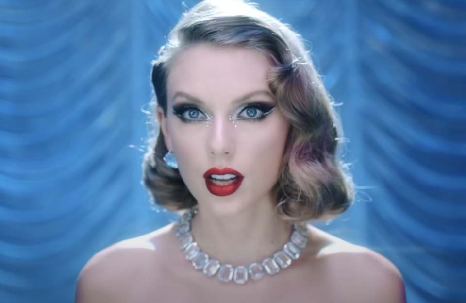 Taylor Swift wearing a glittery dress and necklace, with a blue backdrop