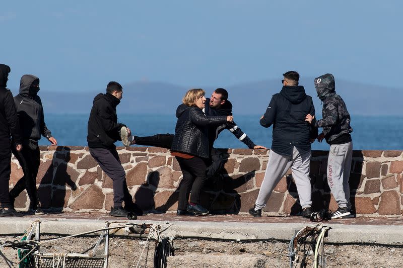 Locals who prevent migrants on a dinghy from disembarking at the port of Thermi beat a journalist, as a woman tries to stop them, on the island of Lesbos, Greece