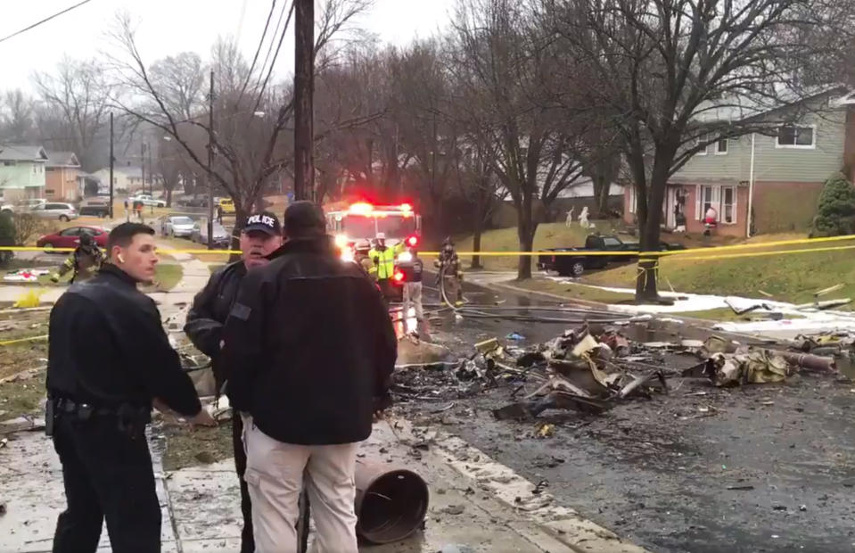 In this image made from video provided by the Prince George's County Fire and Emergency Medical Services Department, firefighters and police officers investigate the scene of a small plane crash in the Lanham neighborhood, Md., Sunday, Dec. 29, 2019. The small plane crashed in the Maryland suburbs of the nation's capital Sunday, hitting a home's carport and killing at least a person aboard the aircraft, authorities said. (Prince George's County Fire/EMS via AP)