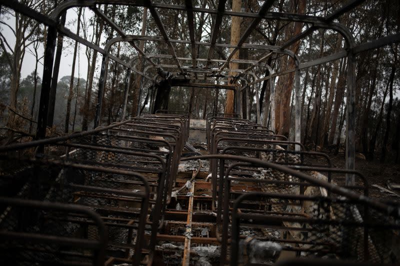 A destroyed bus is seen next to burnt bushland in the village of Mogo