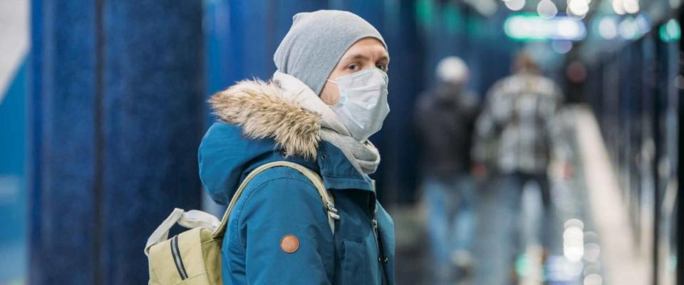 Ill young man feeling sick, wearing protective mask against transmissible infectious diseases and as protection against the flu in public and transportation.